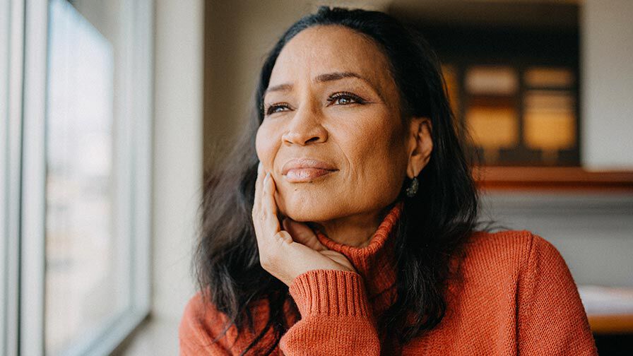 Mulher pensativa a olhar pela janela, ilustra&ccedil;&atilde;o de ansiedade e import&acirc;ncia da sa&uacute;de mental.